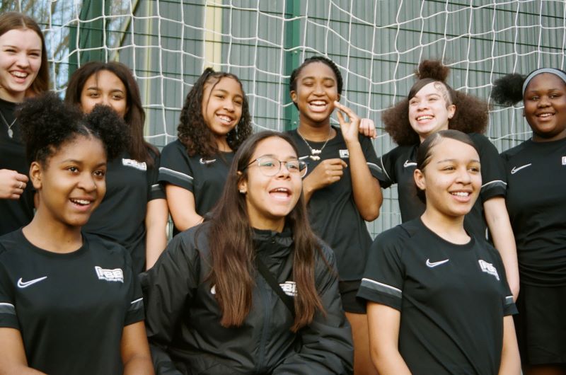 Smiling group of teenage girls in matching sports kit infront of football goal