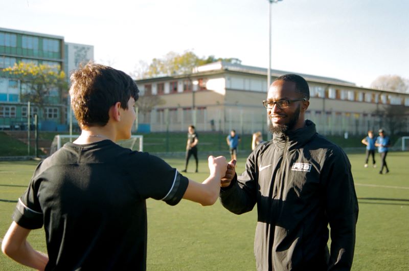 Smiling mentor fit bumping teenager on football pitch