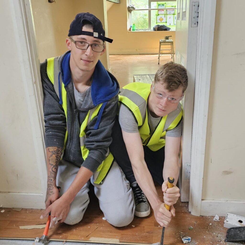 Two young people in high vis holding tools working together on house construction