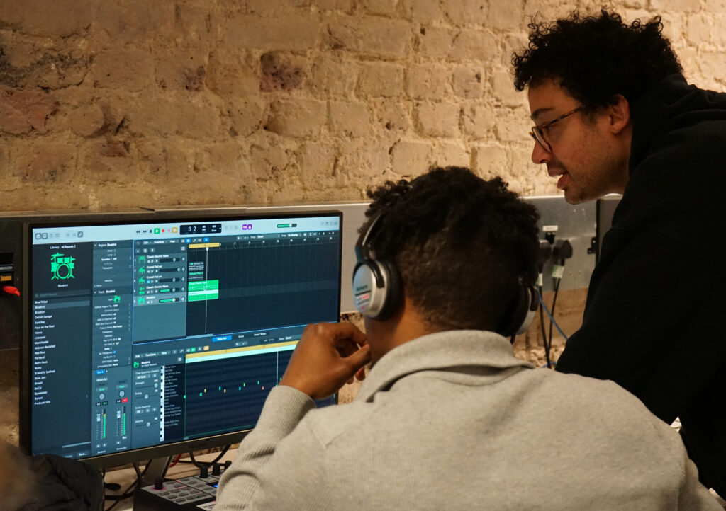 Young person and industry mentor working together infront of computer screen editing music