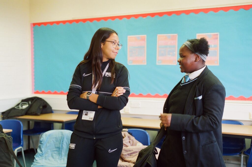 A practitioner from Football Beyond Borders speaks with a student in the classroom.