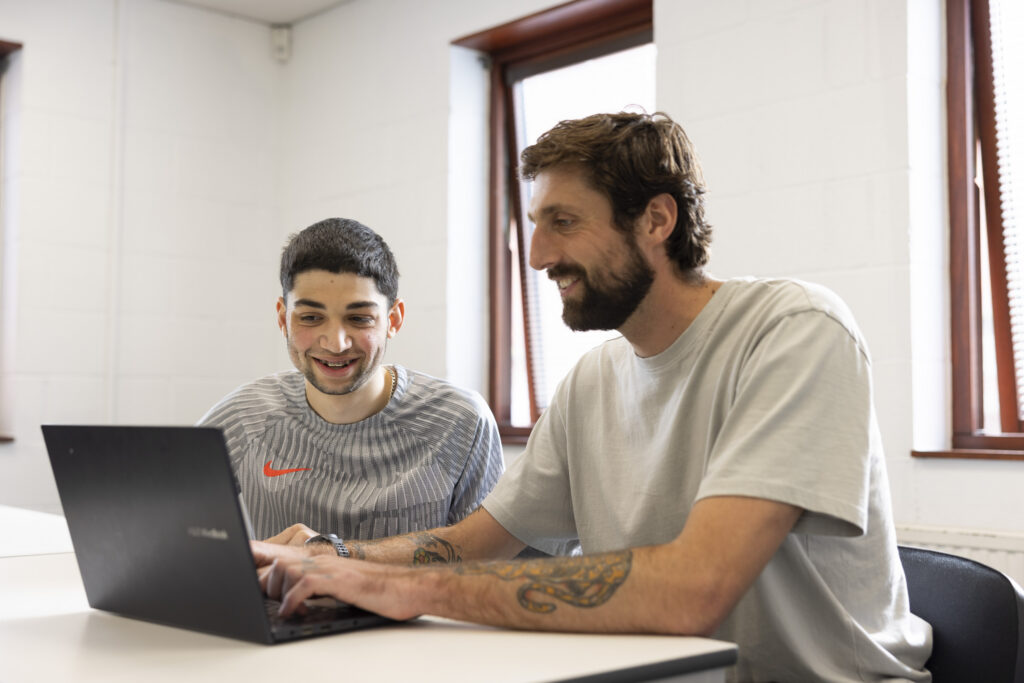 Care experienced young person working with adult coach side by side at laptop. Both are smiling and engaged.